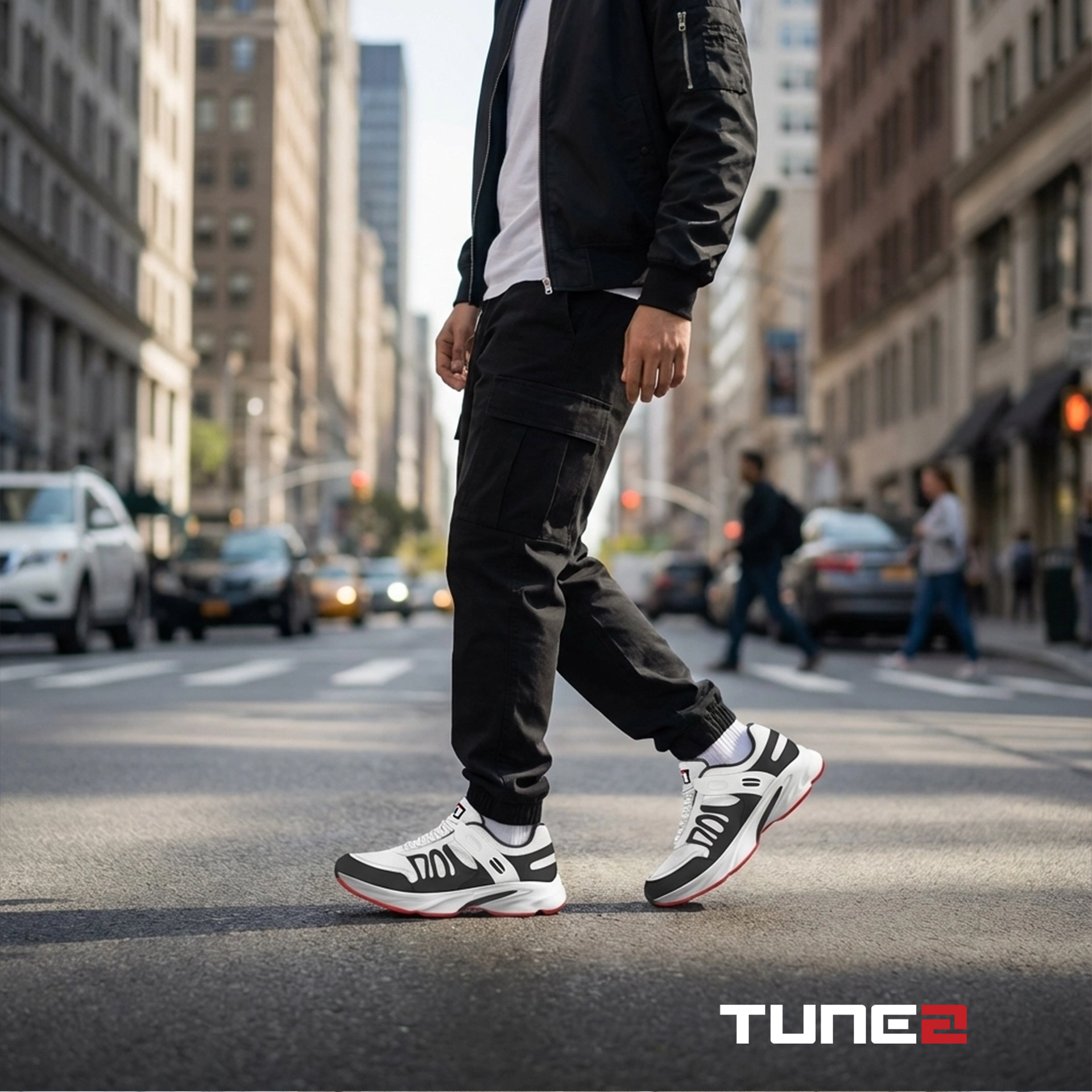 Person walking on a city street wearing black pants and white sneakers with red accents, with 'Tune2' branding.