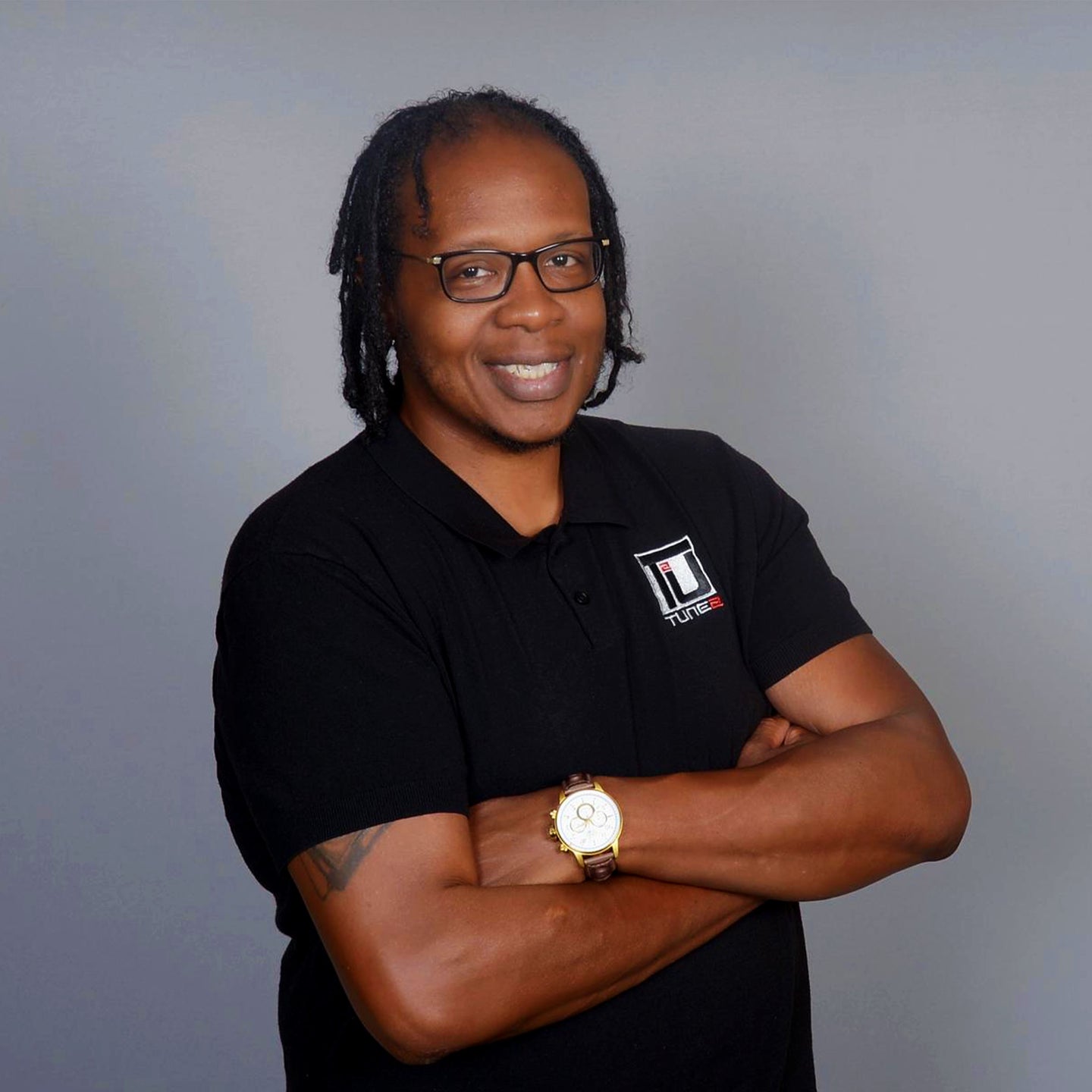 Man wearing a black polo shirt with a logo, standing against a gray background