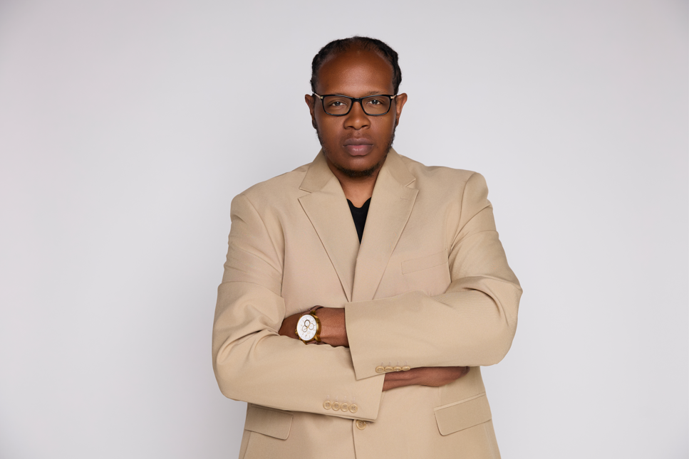Man wearing a beige suit and glasses against a white background