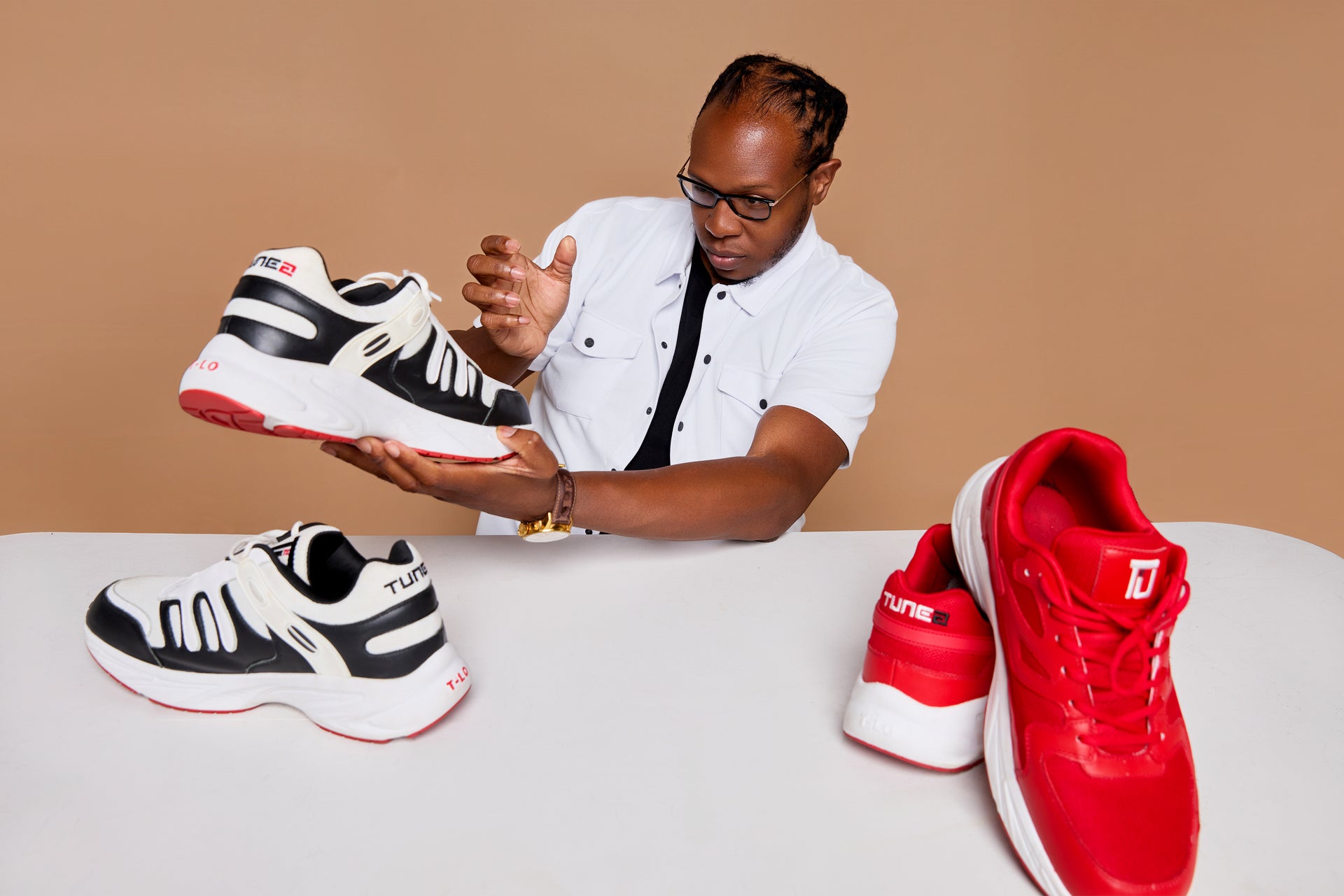 Tunez CEO holding a black and white sneaker with red accents, surrounded by other sneakers on a beige background